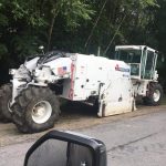 A white utility vehicle being used for construction on an unpaved road.